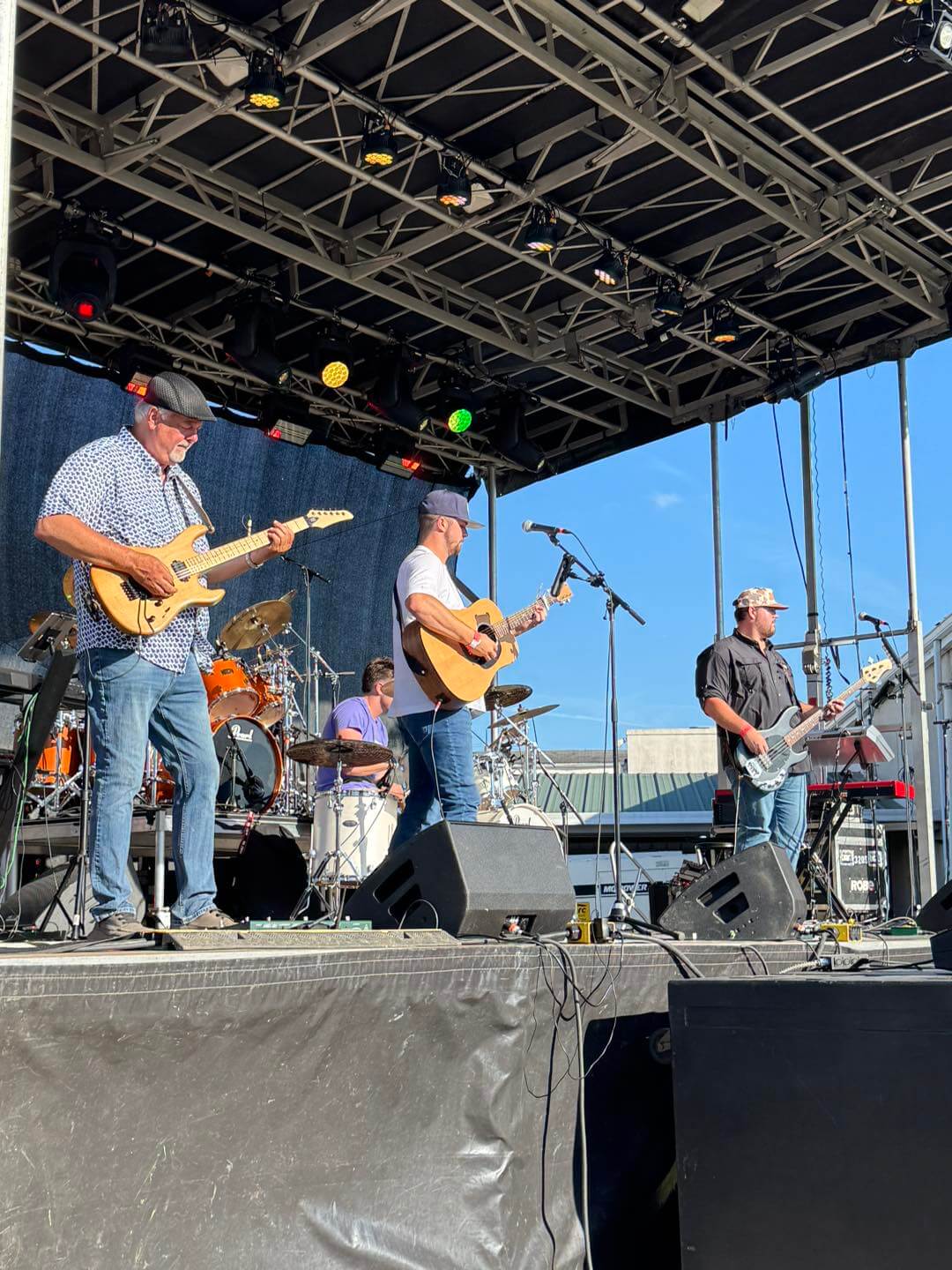 A four-piece band performs on a large outdoor stage at the Red Rose Festival
