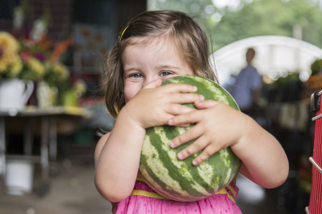 a young girl smiles while holding a watermelon at a festival in the Olde English District