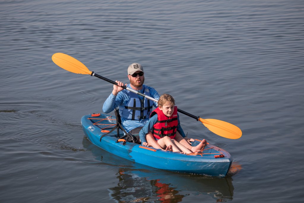 a man paddles a sit-on-top kayak on a lake in the Olde English District as his son sits between his legs